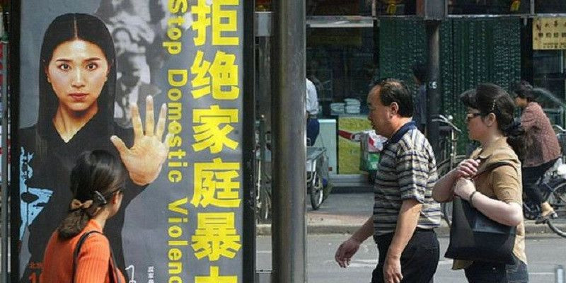 Sejumlah orang melintas di depan poster kampanye yang mendorong stop kekerasan dalam rumah tangga/Net