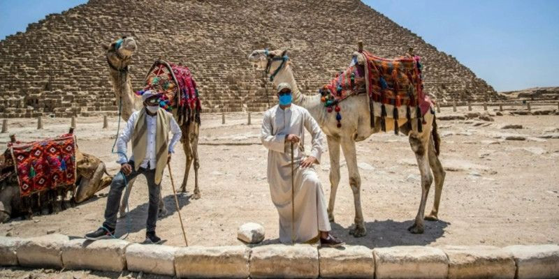 Pemandu unta menggunakan masker di dekat Piramida Agung Khufu (Cheops) di pekuburan Piramida Giza di pinggiran barat daya ibu kota Mesir, Kairo pada 1 Juli 2020/Net